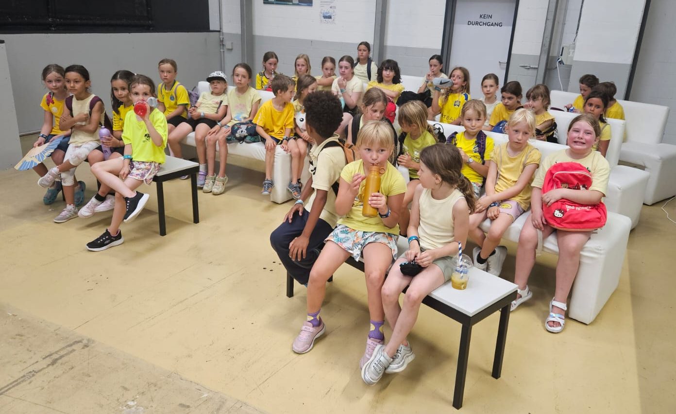 Kinder in gelben Shirts sitzen beisammen und machen bei einem Ausflug Pause